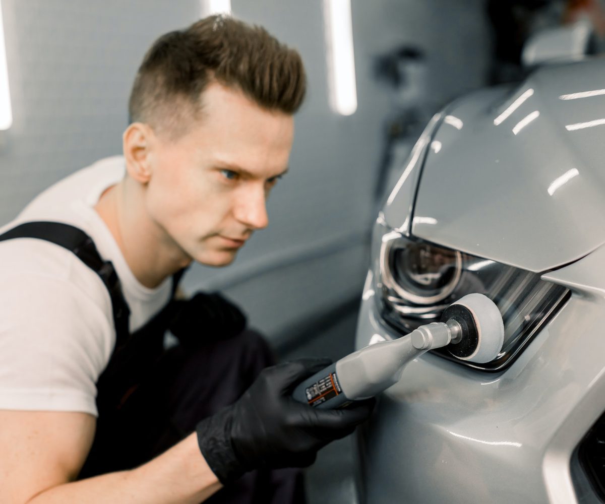 Detailing and polishing of car headlight on car. Young professional concentrated Caucasian male